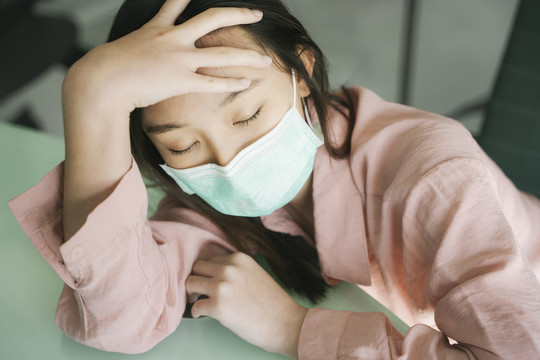病人美丽的亚洲女人戴着医生的口罩，穿着粉色衬衫，躺在医院的桌子上等待医生。