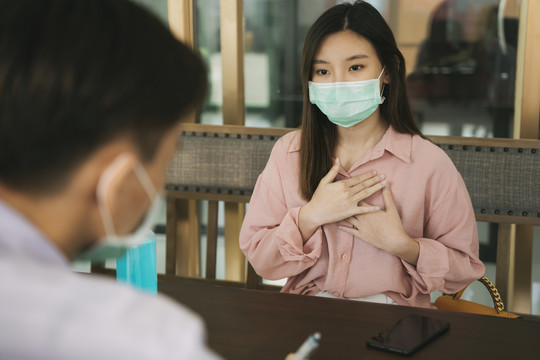 戴着医生口罩的泰国亚裔美女在医院诊断室内与医生谈论Covid-19病毒。