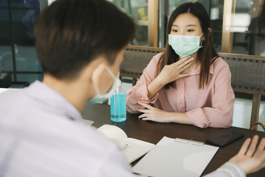 戴着医生口罩的泰国亚裔美女在医院诊断室内与医生谈论Covid-19病毒。