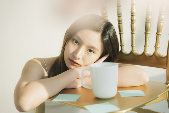 早上，美丽的亚泰女人拿着白咖啡杯躺在椅子上。