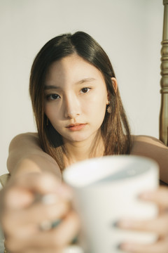 特写亚泰年轻女子手持白色咖啡杯，背景为白色。