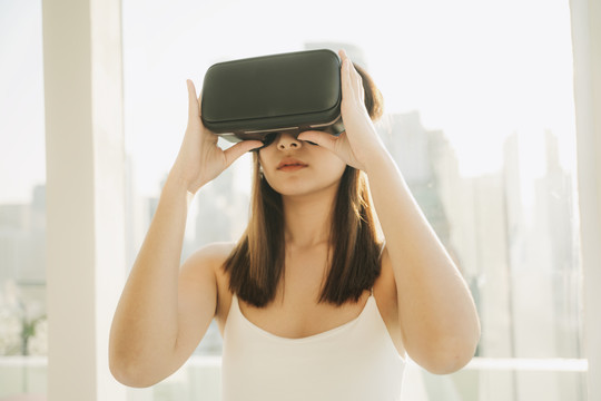 特写美丽的亚泰女子戴着VR耳机，玩虚拟现实游戏。游戏行业的技术。在摩天大楼背景上。