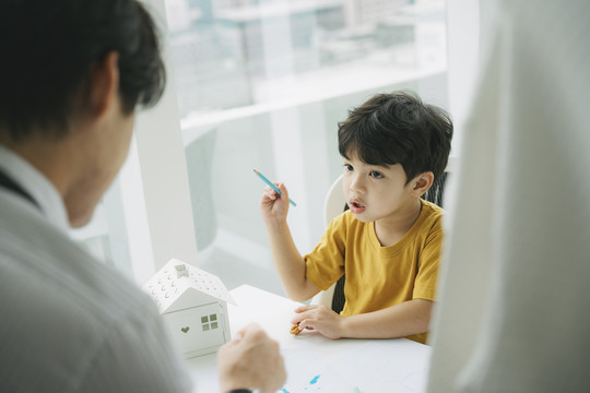 小男孩在客厅的桌子旁做作业，爸爸教他在上班前做功课。