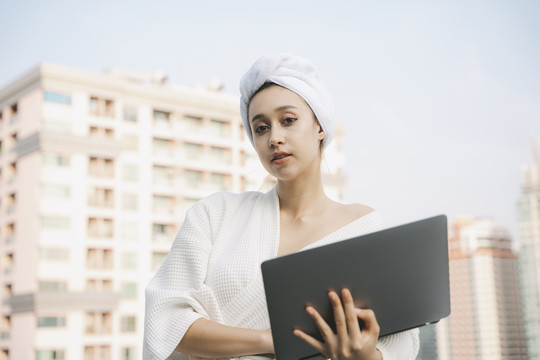 穿着白色浴袍拿着笔记本电脑的年轻女子。在家工作。在Covid-19大流行期间在家工作。