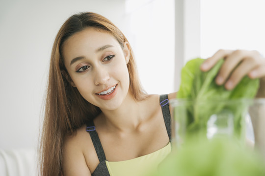 穿着运动内衣的健康年轻女子在厨房用榨汁机勾兑新鲜蔬菜汁，准备营养丰富的维生素包装饮料。健康饮食，素食