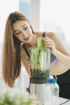 穿着运动内衣的健康年轻女子在厨房用榨汁机勾兑新鲜蔬菜汁，准备营养丰富的维生素包装饮料。健康饮食，素食