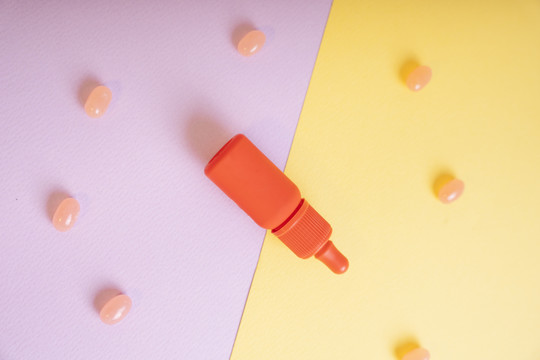 顶视图-橙色瓶包含口红刷黄色和紫色背景与糖果。