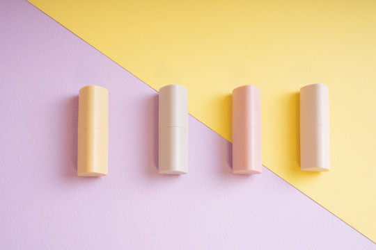 商业产品-黄色和紫色背景的淡米色唇膏组。