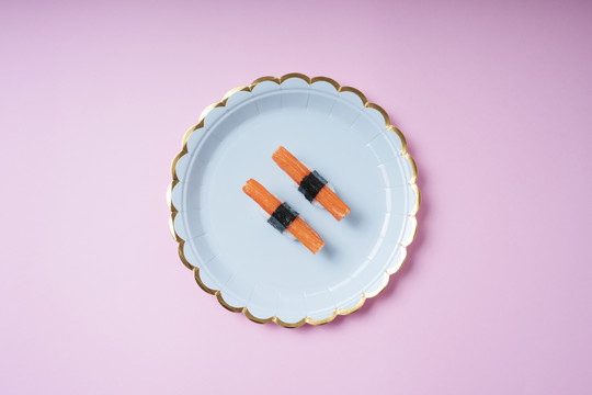 两个蟹棒寿司放在粉红色背景的盘子里。