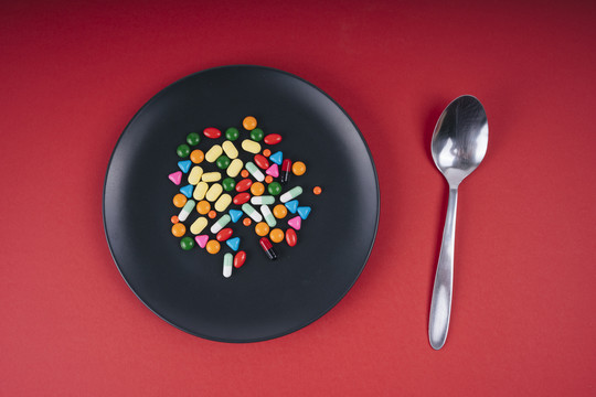 五颜六色的药丸放在黑盘子里，用勺子吃。