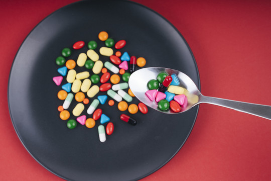 五颜六色的药丸放在黑盘子里，用勺子吃。