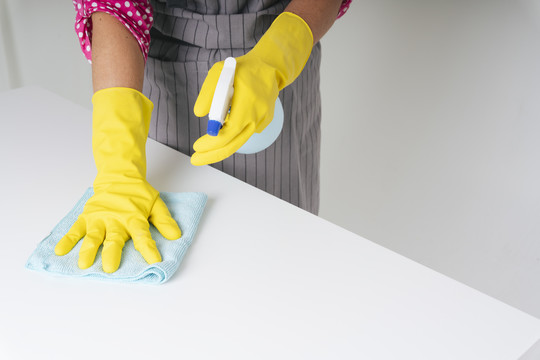 女佣戴手套用抹布和洗涤剂喷雾瓶清洁餐桌。Covid-19冠状病毒预防。