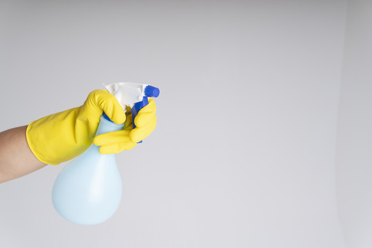 清洁工手戴黄色橡胶防护手套，手拿喷雾洗涤剂瓶。Covid-19冠状病毒预防。