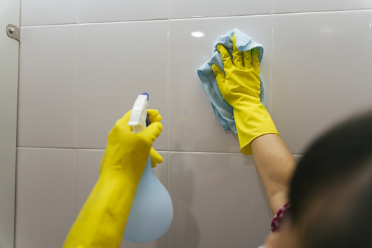 女佣用抹布和喷雾洗涤剂瓶清洁墙壁。Covid-19冠状病毒预防。