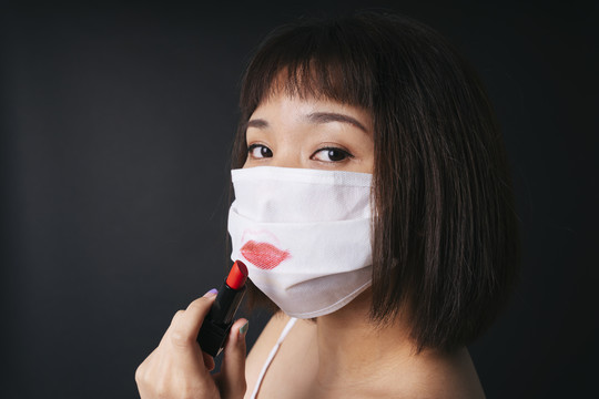 美丽的亚洲泰国女子短发应用红色口红在外科面具隔离黑色背景。美丽的面具。