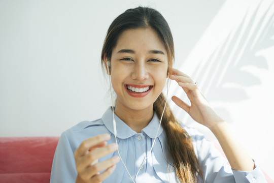 快乐快乐的特写肖像亚泰长发女人大微笑在客厅里用耳机欣赏音乐。