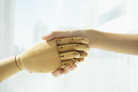木制半机器人的手和人类握手的手。