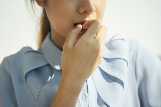 亚洲女人咬指甲。穿着正式衬衫的忧心忡忡的女人的肖像。