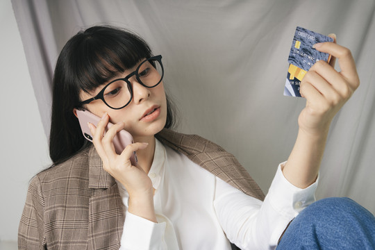 美丽的亚泰黑发女子戴着眼镜手持智能手机和信用卡。商业女性概念。