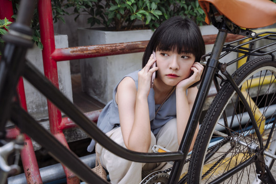 年轻的亚泰妇女旅行时用智能手机打电话给修理工修理坏了的自行车。
