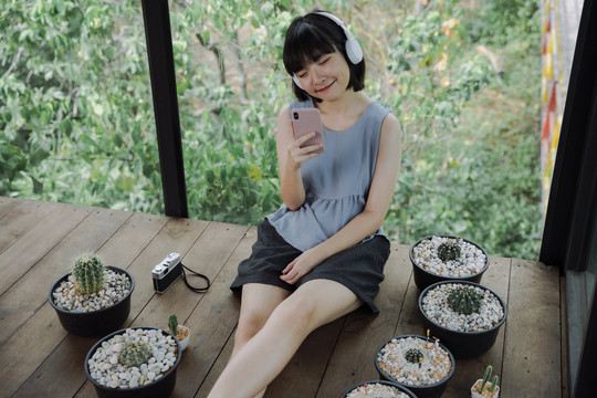 美丽的泰国亚裔女子在当地的仙人掌农场招待所用无线耳机和智能手机欣赏音乐。
