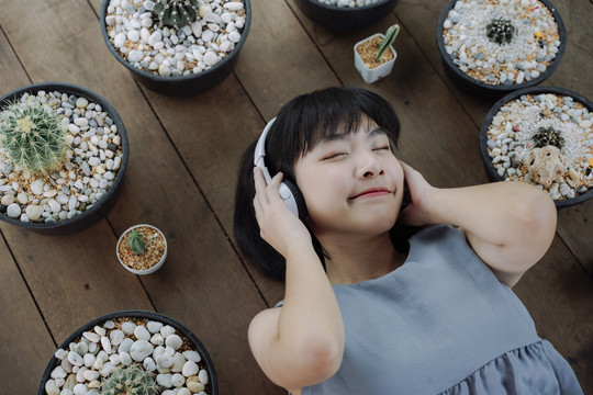 俯瞰图-美丽的亚泰女人深色短发闭着眼睛躺在木地板上用无线耳机听音乐。