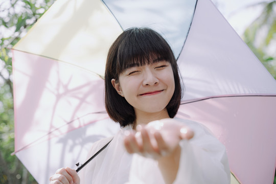 美丽的亚泰女人黑色短发，穿着雨衣，在雨季撑伞。