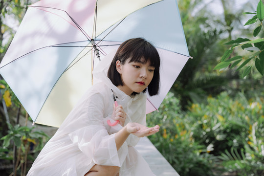 美丽的亚泰女子黑色短发，穿着雨衣，手持雨伞。坐姿。