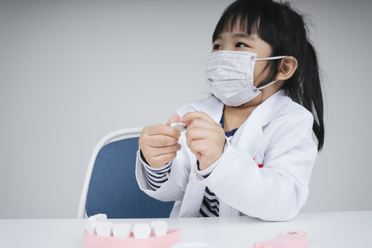漂亮的泰国亚裔小孩扮演医生和牙医戴口罩固定牙齿的玩具。