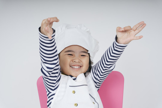 漂亮的泰国亚裔小孩扮演一个厨师的角色，在白色背景下表情欢快。