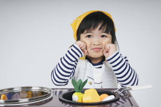 漂亮的泰国亚裔小孩扮演厨师的角色，戴着黄色绷带，在厨房里用炉灶做饭。