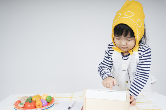 漂亮的泰国亚裔小孩在收银台扮演一个戴着黄色绷带的女服务员。