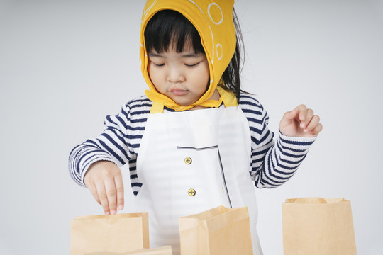 漂亮的泰国亚裔小孩扮演一个穿着黄色绷带的服务员，用纸袋包装食物。