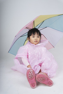 漂亮的泰国亚裔小孩女人穿着粉色雨衣撑着伞。