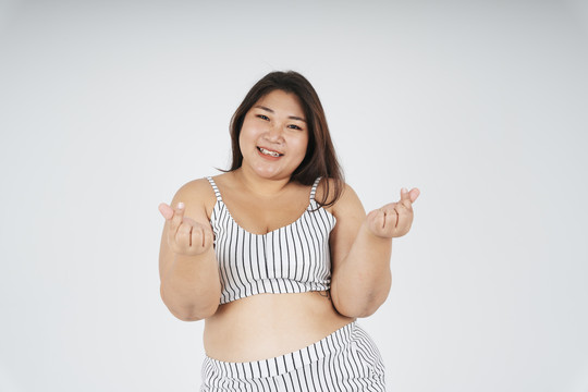 健康的亚洲胖女人的肖像，白色背景上有一个小小的心形手势。