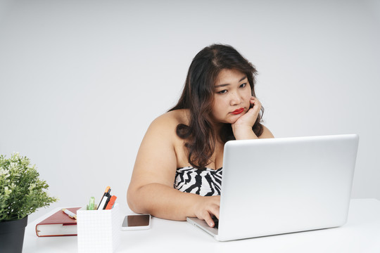 亚洲胖乎乎的女商人，在白色背景的办公桌上拿着笔记本电脑。
