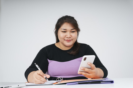 亚洲胖乎乎的女商人在办公桌前拿着白色背景的智能手机。