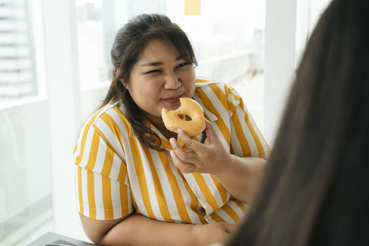 亚洲胖女人喜欢和办公室里的朋友一起吃不健康的甜点甜甜圈。