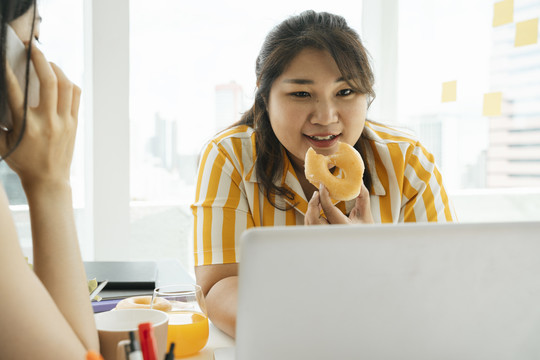 亚洲胖女人喜欢和办公室里的朋友一起吃不健康的甜点甜甜圈。