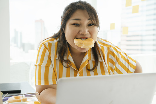 亚洲胖女人喜欢和办公室里的朋友一起吃不健康的甜点甜甜圈。