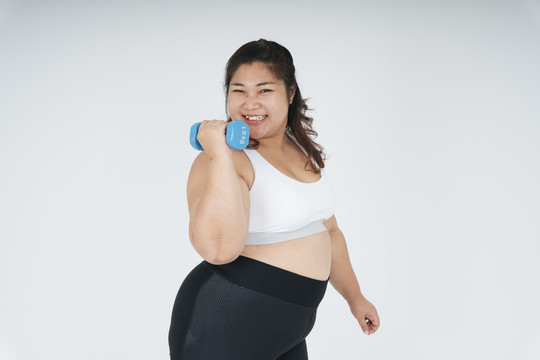 快乐快乐的亚洲胖乎乎的女人，穿着白色运动胸罩，手持白色背景上的蓝色哑铃。
