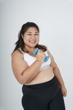 快乐快乐的亚洲胖乎乎的女人，穿着白色运动胸罩，手持白色背景上的蓝色哑铃。