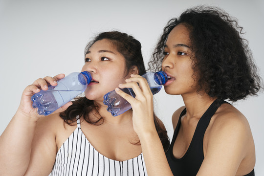 亚洲胖女人和非洲女人一起从瓶子里喝水的特写镜头。