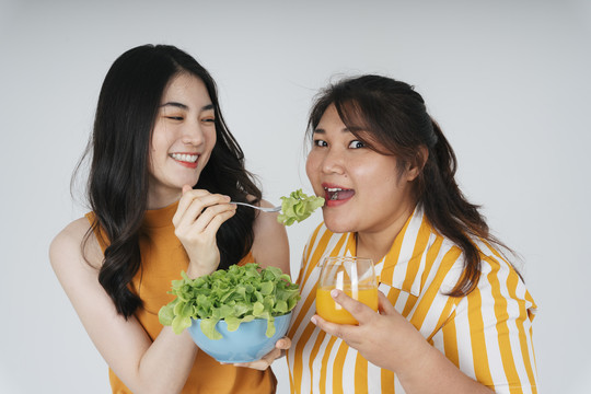 快乐的亚洲女性喜欢吃健康的食物沙拉碗和橙汁隔离白色背景。