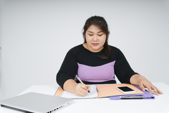 亚洲胖乎乎的女商人在办公桌上写着白纸。