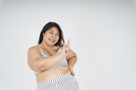 亚洲胖女人的肖像在白色运动胸罩与我爱你手势隔离白色背景。