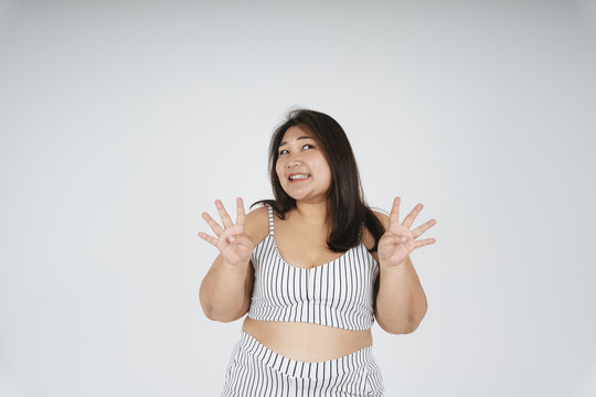 穿着白色运动胸罩的亚洲胖女人的肖像，在白色背景上显示四个手指。
