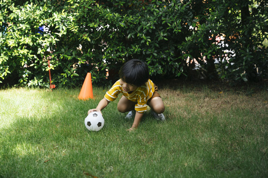 一个亚洲男孩正在摸足球，准备在绿茵场上开球。