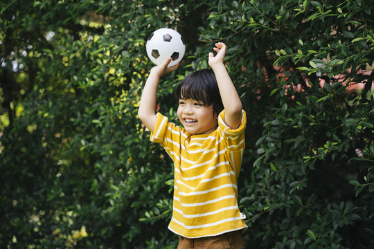 快乐的亚洲男孩在公园举着足球举手。