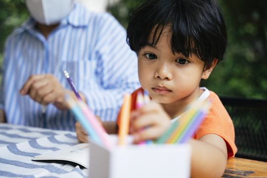 亚洲小孩练习画画，从盒子里挑选彩色铅笔。